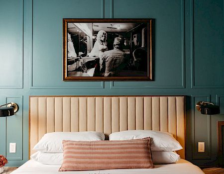 A bedroom with a framed photo above the bed and teal wall panels.