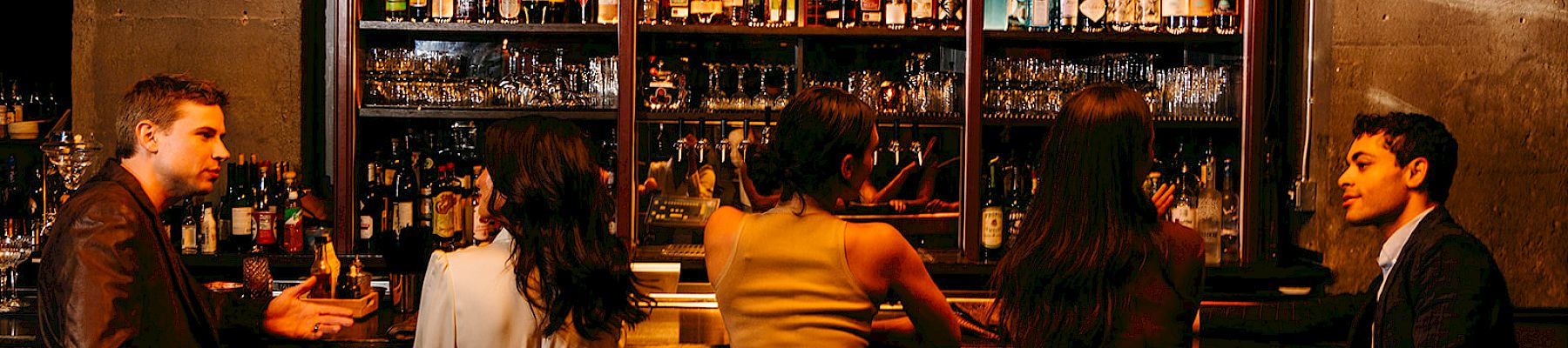 People sitting at a bar with shelves full of bottles.